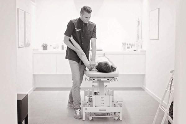 Osteopaat Lieven Van Reybrouck behandelt een patiënt zijn schouder in ruglig op de behandeltafel.
